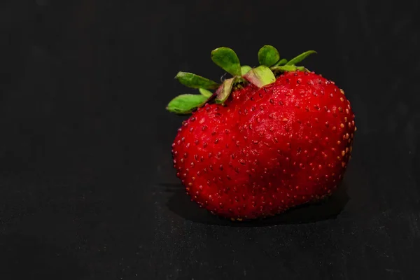 one strawberry on a black wooden background