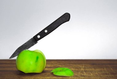 Tahta bir sapla saplanmış bir bıçakla ve tahta bir tahtayı dilimleyen yeşil bir elma.
