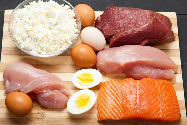 Proteins, fish, cheese, eggs, meat and chicken on a black background — Stock Photo, Image