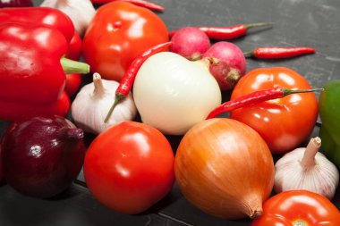 Sebze. Biber, domates, sarımsak, patlıcan, soğan ve turp siyah bir zemin üzerine