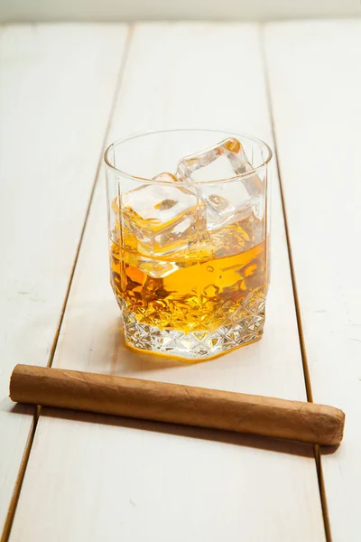 Стакан виски со льдом и сигарой на белом деревянном фоне — стоковое фото