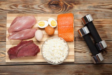 Protein diyeti, balık, peynir, yumurta, et, tavuk ve ahşap arka plan üzerinde halter