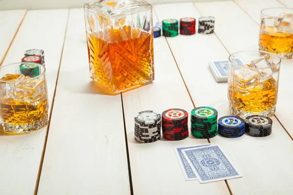 Beyaz ahşap zemin üzerinde buz ile bir bardak viski ve poker oyunu