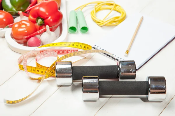 Spor ve diyet. Sağlıklı bir yaşam tarzı. Sebze, halter defter. Biber, domates, sarımsak, soğan turp beyaz arka plan üzerinde bir kalp içinde
