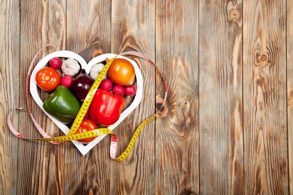 Sport en dieet. Groenten, centimeter. Paprika's, tomaten, knoflook, uien, radijsjes in het hart aan rustieke achtergrond Stockfoto