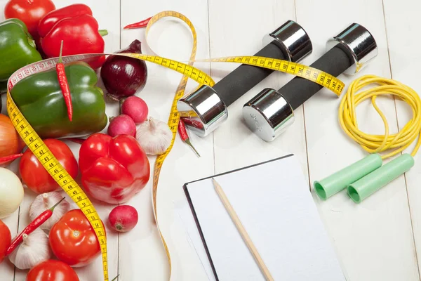 Spor ve diyet. Sağlıklı bir yaşam tarzı. Sebze, halter defter. Biber, domates, sarımsak, soğan turp beyaz bir arka plan üzerinde