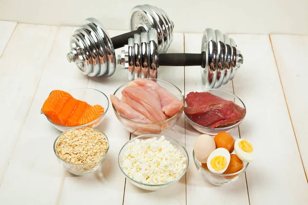 Dieta proteica, pescado, queso, huevos, carne, pollo y pesas sobre un fondo de madera blanco — Foto de Stock