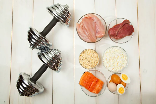 Dieta proteica, pescado, queso, huevos, carne, pollo y pesas sobre un fondo de madera blanco — Foto de Stock