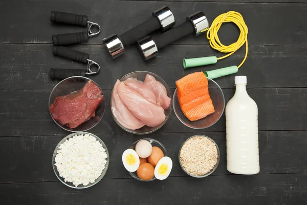 Proteine e manubri. Pesce, formaggio, uova, carne, cuore di pollo su uno sfondo di legno nero — Foto Stock