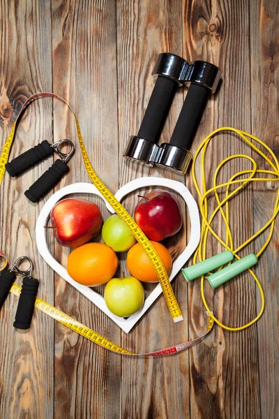 Beyaz kalp, elmalar ve Portakallar, sağlıklı beslenme, dumbell a ahşap arka plan üzerinde ip atlama