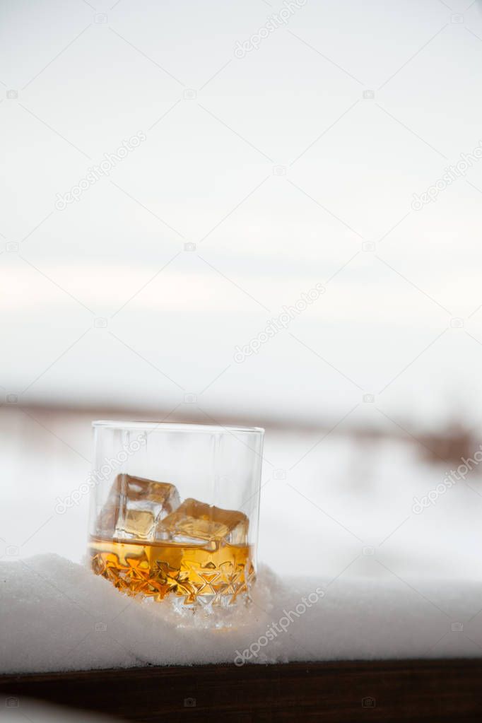 glass of whiskey with ice in snow on winter background.