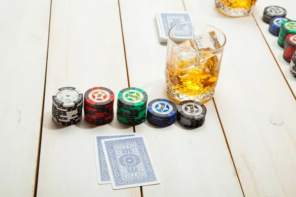 Beyaz ahşap zemin üzerinde buz ile bir bardak viski ve poker oyunu