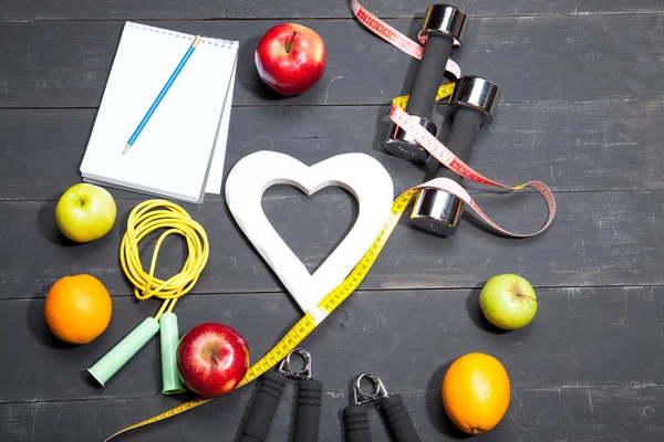 Heart, fruit and dumbbells. Fitness, healthy lifestyle on a black wooden background