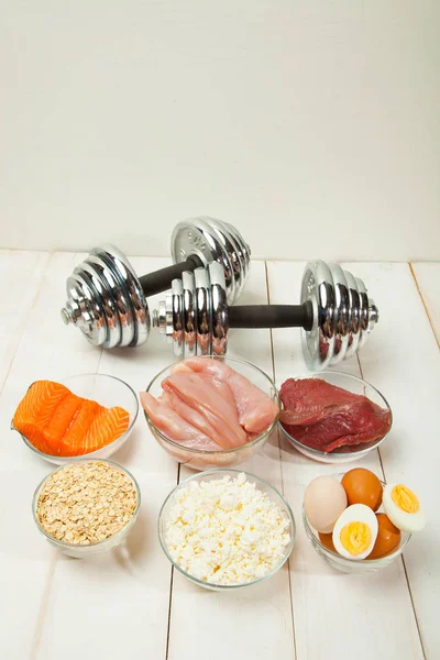 Белковая диета, рыба, сыр, яйца, мясо, курица и гантели на белом деревянном фоне — стоковое фото