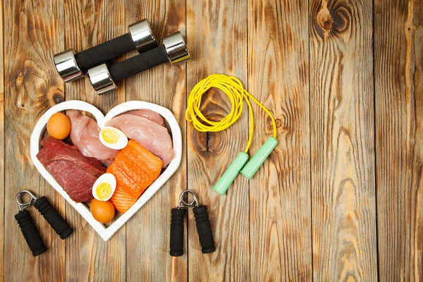 Proteins and dumbbells. Fish, cheese, eggs, meat, chicken  heart on wooden background