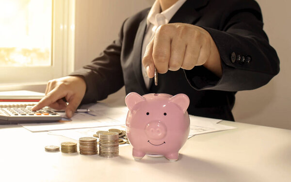Business women who hold coins in a piggy bank closely, including pressing a calculator, saving ideas and saving money for business expenses.