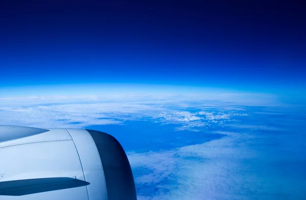 雲の上にある飛行機の窓から外を見ると 飛行機の翼の上に深い青い空とプロペラを持つ白い雲のグループを見た — ストック写真