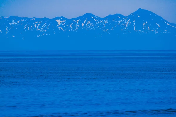 青い海は静かで無人のビーチです 冷たい天気の中で波は穏やかで滑らかです 岩の多い山の向こうで — ストック写真