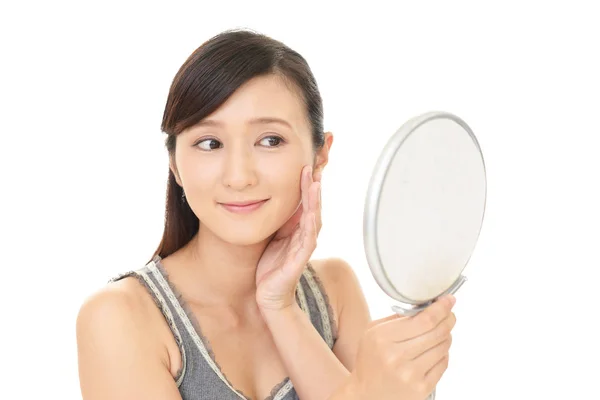 Asian woman looking at her face in mirror — Stock Photo, Image