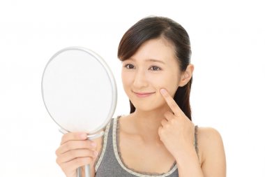 Asyalı kadın aynada yüzüne bakıyor.