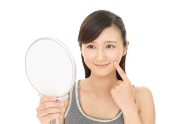 Asyalı kadın aynada yüzüne bakıyor.