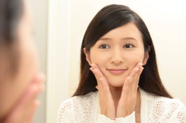 Asyalı kadın aynada yüzüne bakıyor.