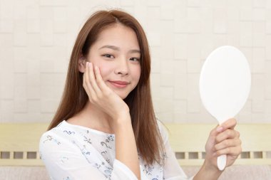 Asyalı kadın aynada yüzüne bakıyor.