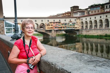 Floransa'daki Ponte Vecchio Köprüsü karşı İtalya'da boynunda video fotoğraf makinesi ile seyahat olgun turist kadın kalır