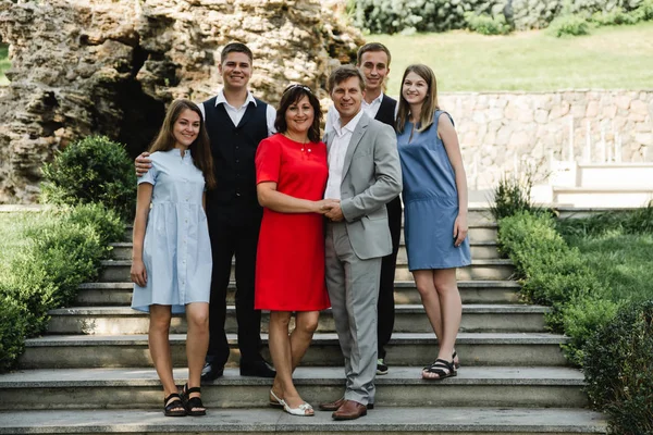 Happy family in dresses and suits posing on the stair. Parents with their adult children walking in the park. Family time and celebrate concept