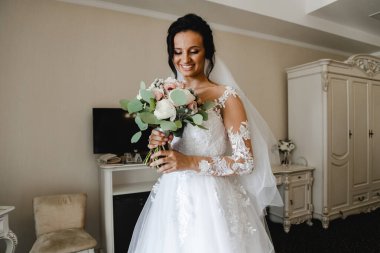 Genç ve güzel gelinin buketli portresi. Düğün günü toplantıları. Güzel bir kız, damadı beklerken bir otel odasında düğün töreni için giyinir ve toplanır. Gelinin sabahı