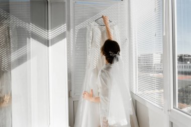 Balkonda genç ve güzel bir gelinin portresi. Güzel kız damadı beklerken dairelerde düğün töreni için giyinir ve toplanır. Gelin elbisesine bakıyor. Gelinin sabahı