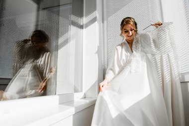 Balkonda genç ve güzel bir gelinin portresi. Güzel kız damadı beklerken dairelerde düğün töreni için giyinir ve toplanır. Gelin elbisesine bakıyor. Gelinin sabahı