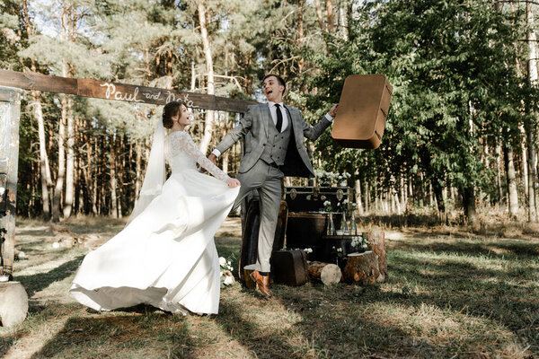 Attractive couple celebrating their wedding in forest. Portrait of young happy groom and bride in wedding clothes standing together, holding hands and looking at each other near wedding photozone