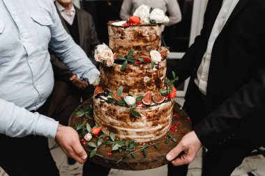  Güllerle süslenmiş zarif bir düğün pastası ve arka planda gelin ve damat olan meyveler. Düğün töreni. Masada güzel bir turta var. Gelinler pastayı birlikte keserler. Kapat.