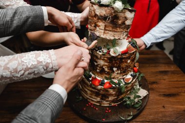  Güllerle süslenmiş zarif bir düğün pastası ve arka planda gelin ve damat olan meyveler. Düğün töreni. Masada güzel bir turta var. Gelinler pastayı birlikte keserler. Kapat.