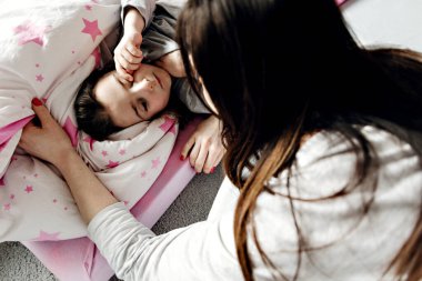 Anne ve kızı sabah, genç anne kızı battaniyeye sarılı bir şekilde yerde yatıyor, mutlu anne kızına hayran, kızının annesiyle olan ilişkisi.