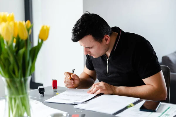 Ciddi bir adam masaya oturur ve evrakları dolgu kalemiyle doldurur. Evrakları doldurur, uzaktan kumanda eder, serbest çalışır, belge hazırlar.