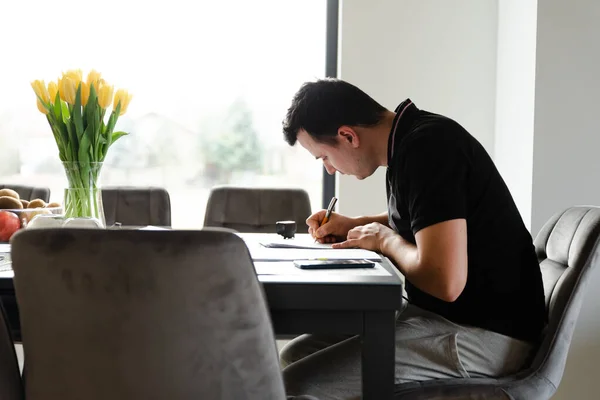 a serious man sits sitting at a table and fills out documents with a pen,filling out documents,remote business,self employed,working person for documents