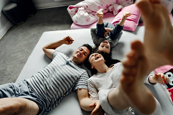 Sevimli küçük bir kızın ve güzel anne babasının kameraya bakıp gülümsemesi, evde yerde yatması, dinlenen bir ailenin yerde yatıp kameraya bakması.