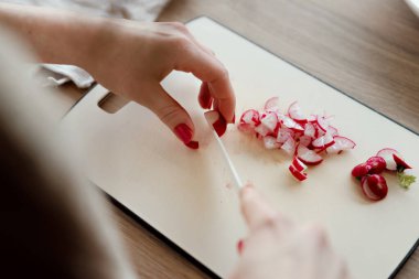 Bir kız taze bahar salatası için tahtada turpla bıçak kesiyor mutfakta taze turp dilimleyen bir kadın, marul kesmek için güzel bir bıçak.