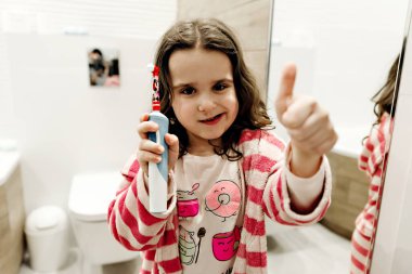 Güzel bir banyoda dişlerini güzel bir dişle fırçalıyor, bornozlu genç bir kız geceleri dişlerini fırçalıyor, diş macununu bir kızın elinde tutuyor.