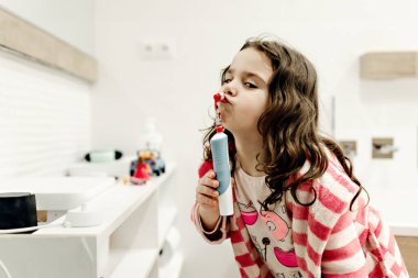 Güzel bir banyoda dişlerini güzel bir dişle fırçalıyor, bornozlu genç bir kız geceleri dişlerini fırçalıyor, diş macununu bir kızın elinde tutuyor.