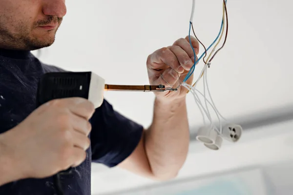 electrician,a male electrician is standing on the stairs holding wiring in his hands and stripping,repairing light at home,wiring in hands corrects construction problems,repair work,call master,electrician man repairing light