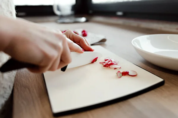 a girl cuts a knife with radish on a board for fresh spring salad,woman slicing fresh radish at home in kitchen,beautiful knife for cutting lettuce