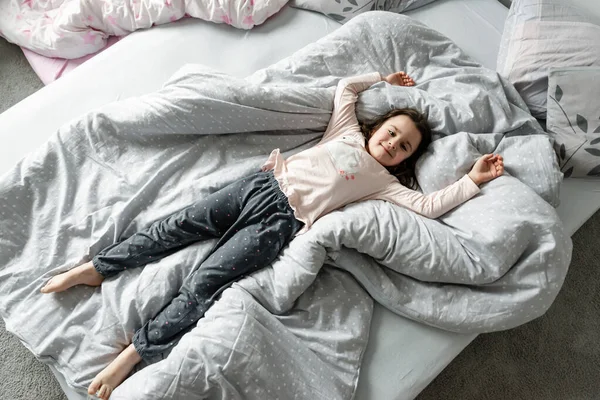 girl on the bed,top view of the girl who is in bed,girl lying and indulging in bed in the morning after waking up,happy child,the child indulges and rejoices,the baby is lying on the bed
