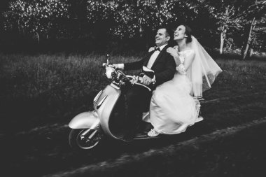 Düğün damadı ve gelin motosiklet sürüyor, eğleniyor, gülümsüyor düğün çifti gün batımında şehir dışındaki yolda scooter 'a biniyor, düğün çifti scooter' a biniyor, yeni evliler dekore edilmiş scooterla eğleniyor, bulanık yeni evliler.