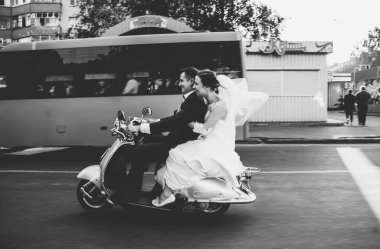 Düğün damadı ve gelin motosiklet sürüyor, eğleniyor, gülümsüyor düğün çifti gün batımında şehir dışındaki yolda scooter 'a biniyor, düğün çifti scooter' a biniyor, yeni evliler dekore edilmiş scooterla eğleniyor, bulanık yeni evliler.