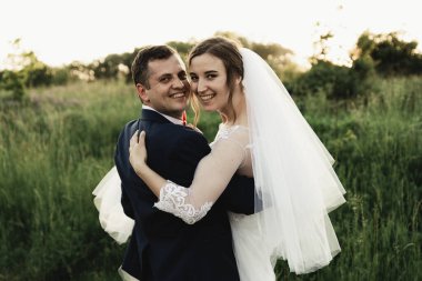 Mutlu damat yaz parkında gelin yetiştiriyor. Adam kadını kollarına alıp kucakladı. Parkta yeni evli bir çift. Yeni evlendim. Parkta yürü ve sarıl. Yeni evliler eğleniyor. Kırsal düğün