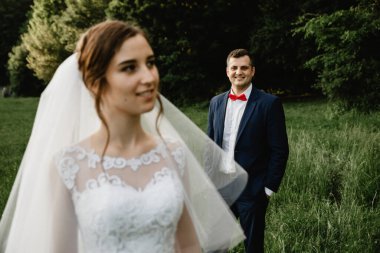 Gelin ve damat gün batımında kucaklaşıyor. Mutlu gelin ve damat gülümsüyor. Düğün gününden sonra mutlu gelin ve damat. Çiçekli bir tarlada güzel bir çift, ormanda genç bir çift, doğada gelin ve damat.