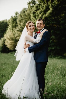 Gelin ve damat gün batımında kucaklaşıyor. Mutlu gelin ve damat gülümsüyor. Düğün gününden sonra mutlu gelin ve damat. Çiçekli bir tarlada güzel bir çift, ormanda genç bir çift, doğada gelin ve damat.